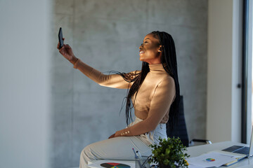 A confident businesswoman with a radiant smile engages in a video call, dressed professionally,...