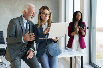Obraz premium A mixed ethnicity group with a man and two women in professional attire examines data on a laptop in a bright office setting, reflecting teamwork and collaboration.