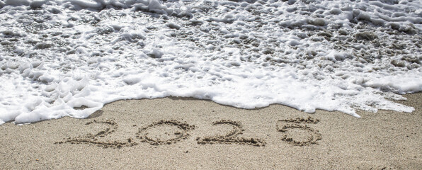 tropical New Year 2025 written in sand on the beach