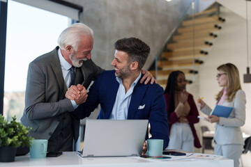 A focused male Caucasian executive browses data on his laptop in a modern office setting, professional attire evident, with colleagues in the background.