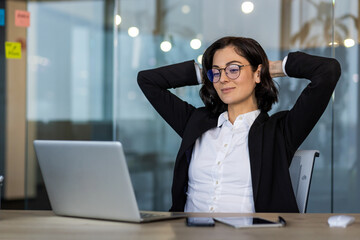 Young businesswoman relaxing at desk with laptop and phone in office. Confident and composed, she...