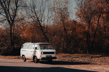 Fototapeta premium Vintage white van parked by a roadside under autumn trees, capturing a nostalgic, travel-ready moment in the fall.