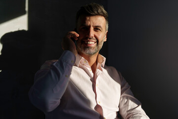 A cheerful mid adult Caucasian businessman engages in a phone conversation, sporting professional attire, with an office backdrop subtly suggesting a corporate setting.