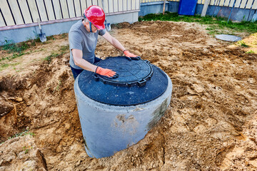 Mature male builder installed manhole cover on concrete septic tank ring.