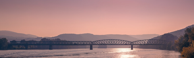 Two bridges are crossing the danube river in krems an der donau, austria, during a colorful sunset with hills in the background