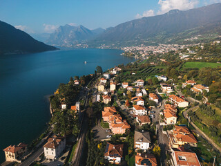 Aerial view of a scenic lakeside town surrounded by lush green hills and mountains, with red-roofed...