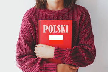 one girl schoolgirl in burgundy sweater holds red polish language textbook with Poland flag and...