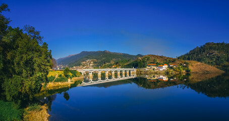 White bridge reflecting in the calm water of the Cavado river, in Rio Caldo, surrounded by lush...