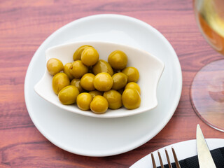 White bowl filled with marinated green olives as tangy and savory snack for wine. Mediterranean gastronomic culture