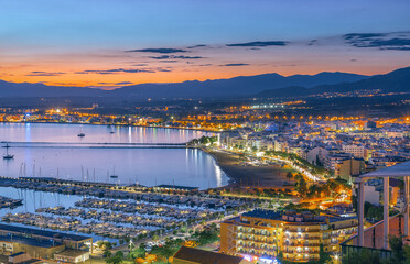 Roses, spain comes alive at sunset, with the warm glow illuminating the cityscape, harbor, and boats, creating a picturesque scene of coastal beauty