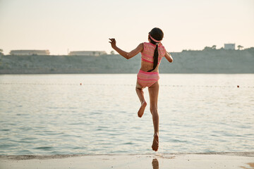 A young girl wearing swim goggles playing on rocks and jumping into water