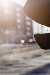 close-up of car exhaust pipe against the backdrop of urban development, on a frosty winter morning against the backdrop of bright sun