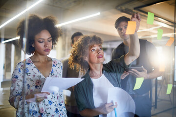 Young people placing sticky notes on a window in the startup company office