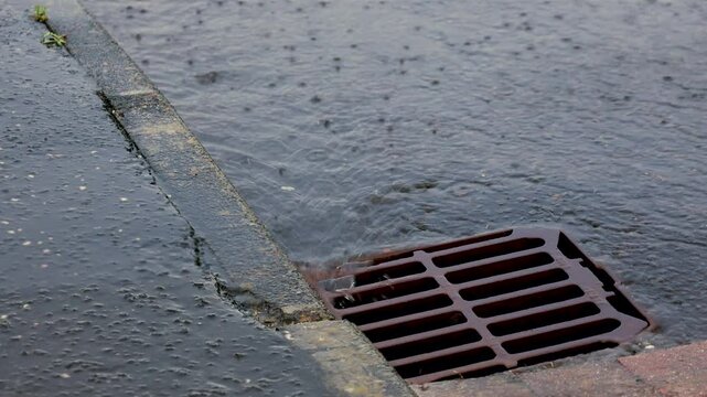 Rain water running into storm sewer drain on road during extreme weather heavy rainfall