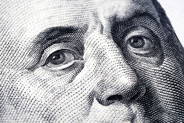 The macro photograph features an extreme close-up of Benjamin Franklin's eyes from the portrait on the U.S. one-hundred-dollar bill. Engraving details, including the fine lines and dot patterns. 