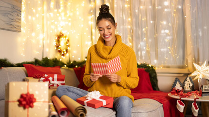 Happy lady reading Christmas card or letter in home living room in winter holiday celebration, woman with emotional Xmas greeting message, wishes or kind gift