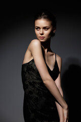 Naklejka premium Elegant young woman posing in a dark, sophisticated black dress against a soft gray background, showcasing a confident and artistic expression.