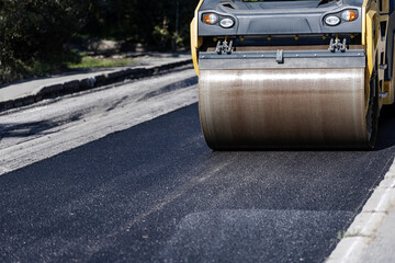 A steamroller compacts freshly laid asphalt on a sunny day in a residential area, showcasing road...