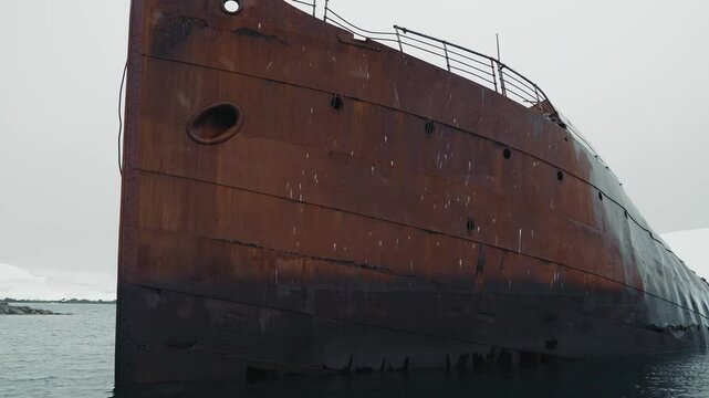 A rusted whaling ship is stranded in the icy waters of Antarctica, in the Southern Ocean. Its weathered hull contrasts with the frozen landscape, creating a haunting scene in the remote wilderness.