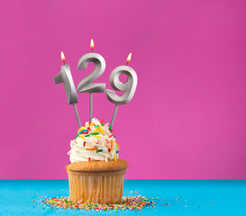 Lit birthday candle with the number 129 - Celebration card on violet and blue background