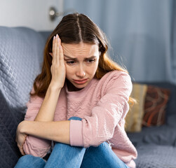 Portrait of a frustrated young European woman sitting on a sofa in an apartment