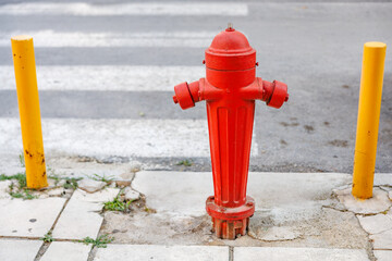 A red fire hydrant is on the sidewalk next to a yellow pole