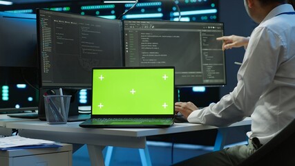 Zoom in on green screen laptop used by data center worker troubleshooting issues. Engineer uses chroma key notebook in server hub, establishing performance benchmarks, camera A