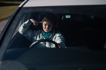 Caucasian woman twirls finger at temple while driving. 