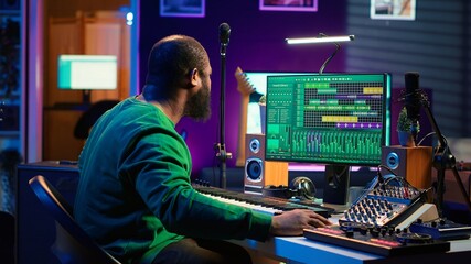 Audio composer playing piano electronic keyboard to create a new track, adjusting volume levels on...