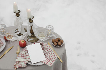 Christmas festive outdoor table setting. Dinner arrangement. Glass of wine, candles, golden cutlery. Checkered napkins. Winter wedding, Valentines day. Blank menu card mockup, blurred snow landscape.