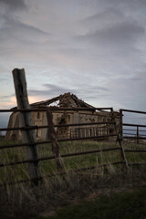 old abandoned dovecote with a partially collapsed roof, set against a dramatic evening sky. The surrounding grass and distant buildings add a rural charm, highlighting the beauty of decay and solitude