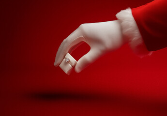Santa's hand in a white glove holding an engagement ring  on a red background.Minimal creative Christmas holiday fashion jewelry advertise concept.Copy space,flat lay 