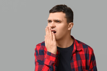Handsome young man feeling bad smell from mouth on grey background
