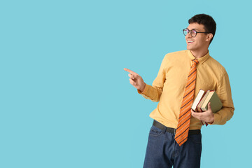 Smiling young man with striped tie and books pointing at something on blue background