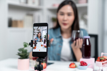 Selective focus smartphone with smiling young beautiful Asian reviewing mixed strawberry and cherry...