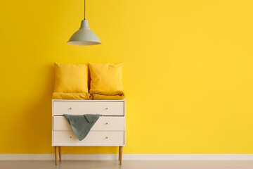 Pillows with folded blankets on commode near yellow wall in room