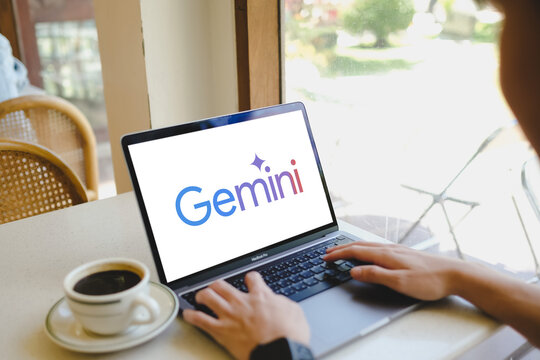 Bangkok. Thailand. November 6, 2024 : A man using a laptop with a "Gemini" is Ai open chatl ogo of google on the screen while sitting at a desk near a window with a cup of iced coffee.