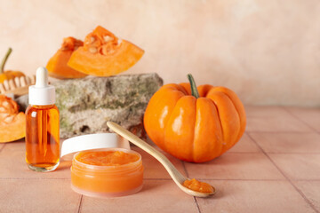 Jar of cosmetic pumpkin mask and bottle of oil on beige tile table