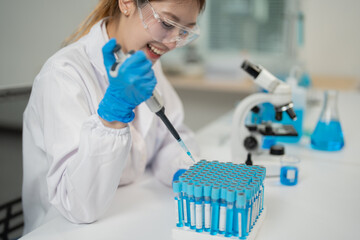Smiling scientist wearing lab coat and gloves using micropipette to analyze samples in test tubes,...