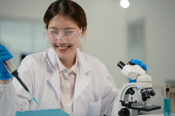 Asian female scientist wearing lab coat, safety goggles and gloves, smiling and using micropipette...