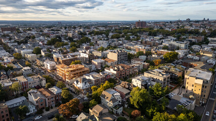 Fototapeta premium Wide aerial view capturing the neighborhoods of Hoboken and Jersey City, with the iconic New York City skyline stretching across the horizon in the background. Overcast skies add depth 