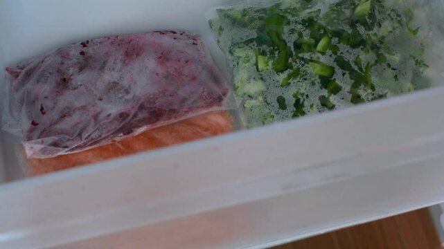 Hand opens drawer in the freezer containing bags of chopped vegetables.