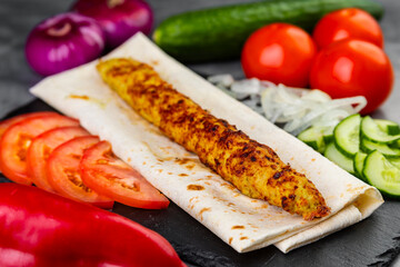 Grilled lula kebab on skewers with spices and vegetables in a black plate on a gray background