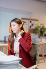 Young asian businesswoman massaging her neck suffering from stiff neck after working on computer...