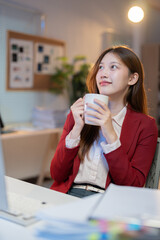 Young asian businesswoman holding a coffee cup and thinking about new project while working late in...