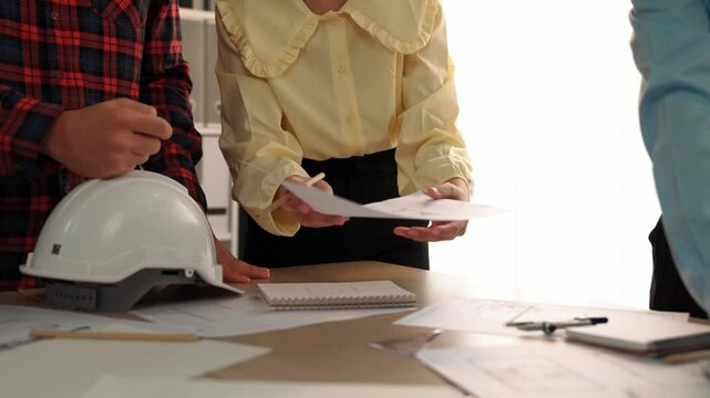 Architect and safety engineer discussion about building blueprint displaying on laptop on table with architectural document and wooden block scatter around at modern office. Closeup. Delineation.