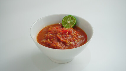 Sambal Tomat or Spicy Tomato Paste served on the bowl, kaffir lime slices on the side. Sambal made of chili, garlic, onion and tomato.