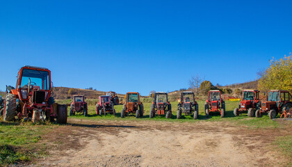 A group of many old agricultural tractors parked on a field. Farm tractors abandoned