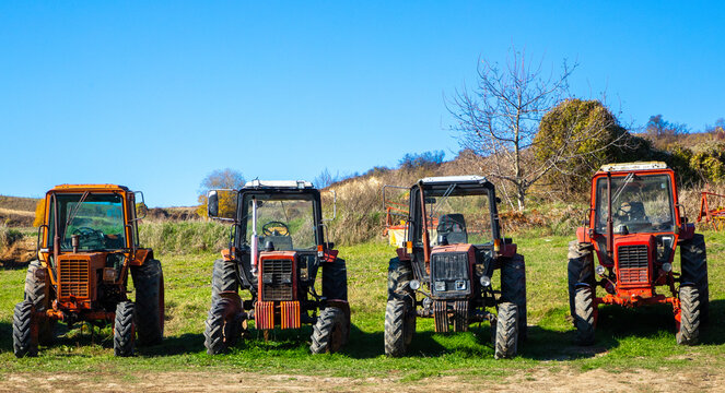 Many old agricultural tractors parked in a row on a field 