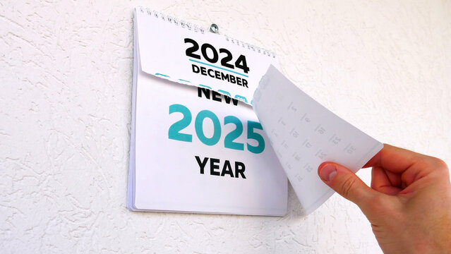 A man's hand tearing off the December page of a wall calendar followed by another announcing the arrival of the New Year 2025